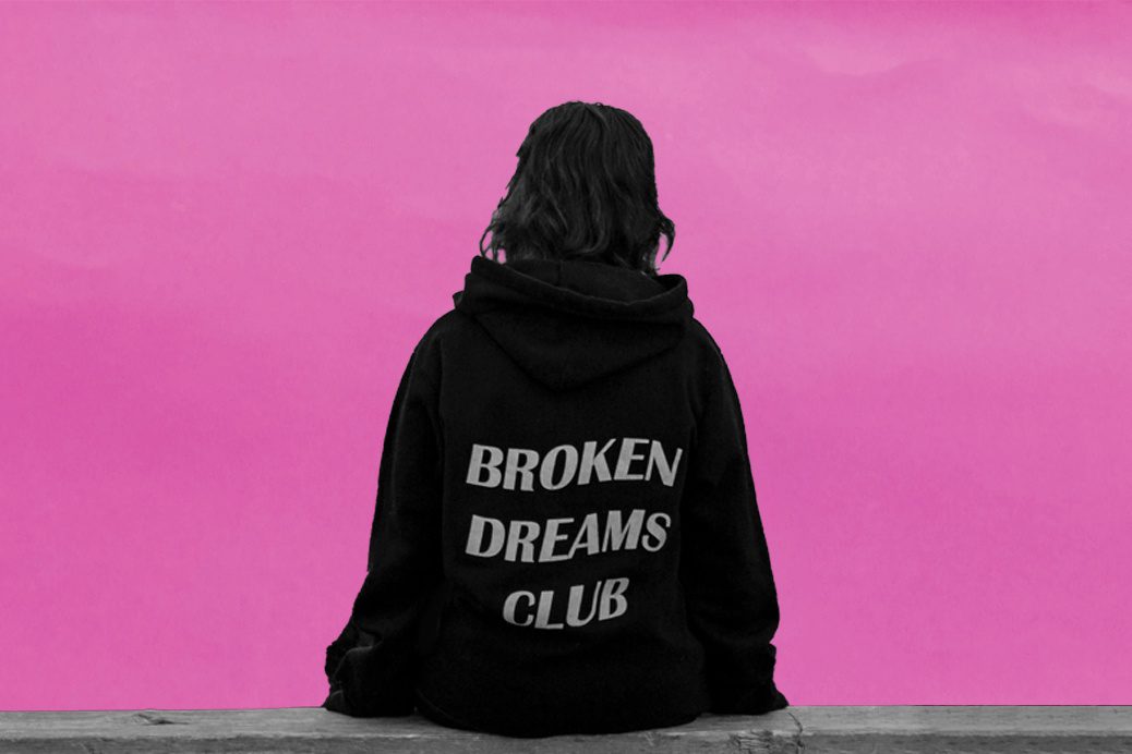 Women sitting on a bench with the words 'Broken dreams club' on her jumper.
