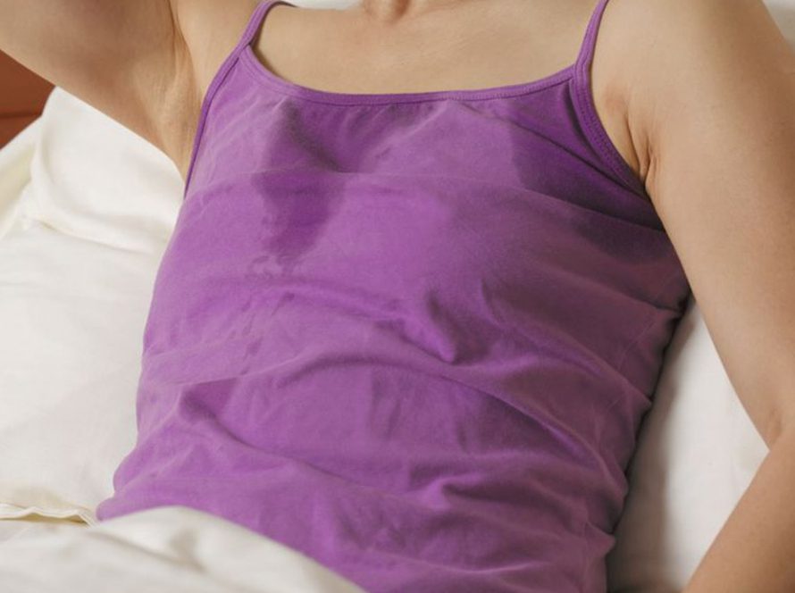 Women lying in bed wearing a purple top sweating