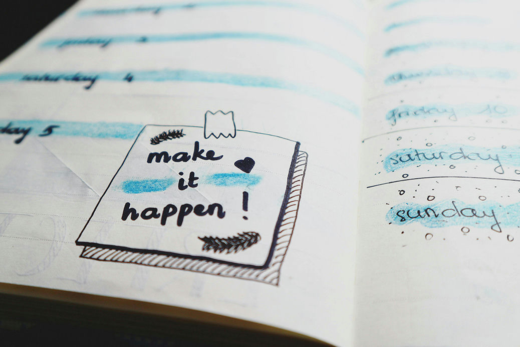 A low angle shot of a notepad with a sketch of a post it note that reads "make it happen"